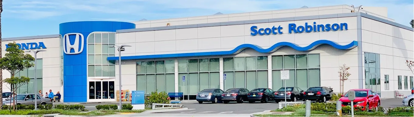 Exterior of Scott Robinson Honda dealership with people seated outside and cars parked in front.